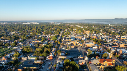 Obraz premium Aerial view of Carlisle, PA, showcasing a mix of residential, commercial buildings, and tree-lined streets under a clear morning sky.