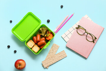 Lunch box with tasty food and school stationery on blue background