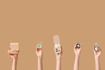 Female hands with different palettes of eyeshadows on brown background
