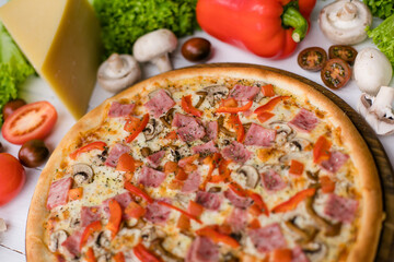 Delicious fresh Pizza with tomatoes, mashrooms, bacon and cheese mozzarella on the white wooden table.