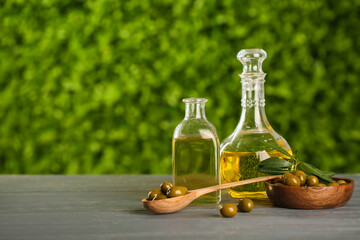 Decanter and bottle of fresh olive oil on grey wooden table outdoors