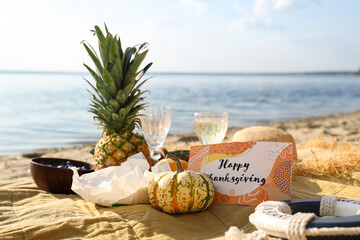 Pumpkin, pineapple, wine and greeting card with text HAPPY THANKSGIVING DAY on beach