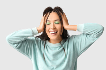 Happy young Asian woman with stylish mint makeup on grey background