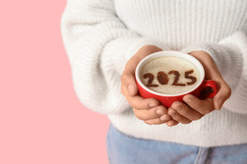 Woman holding cup of coffee with figure 2025 on pink background, closeup