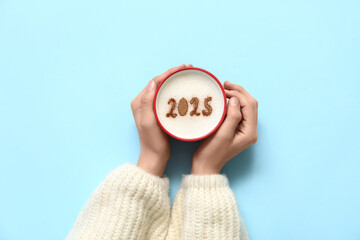 Female hands and cup of coffee with figure 2025 on color background, closeup