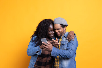 African american husband and wife having fun with social media videos on phone against yellow...