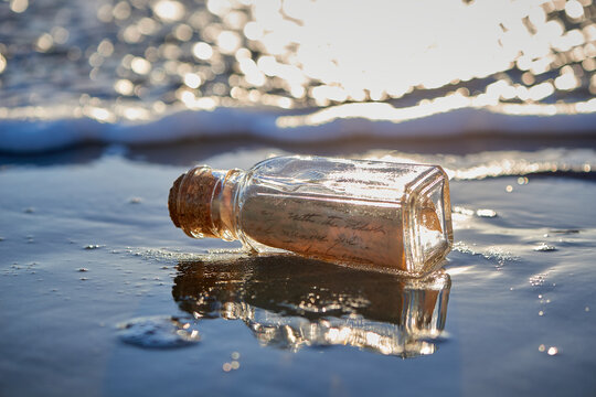 Handwritten letter message in glass on bottle washed up on sand beach with waves and ocean water in the background. 