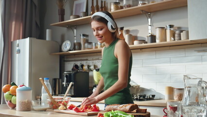 Headphones woman chopping vegetables in home kitchen. Joyful girl cooking salad