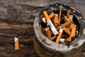 Closeup of an ashtray filled with numerous cigarette butts on a wooden surface, symbolizing smoking habits and litter, smoking harm, urban pollution, unhealthy lifestyle, littering.
