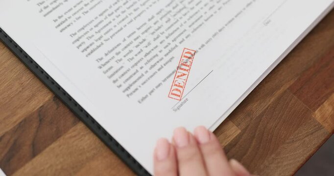 Woman employee hand puts stamp with Denied mark on documentation at workplace. Female worker prepares documentation refusing offer in office