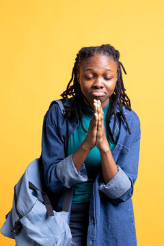 Religious african american young girl with eyes closed praying to her god. Spiritual BIPOC teenager doing worship hand gesturing, waiting for miracle, doing confession, studio background