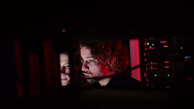 A man and a woman trying to fix an error in a server room with flashing red lights