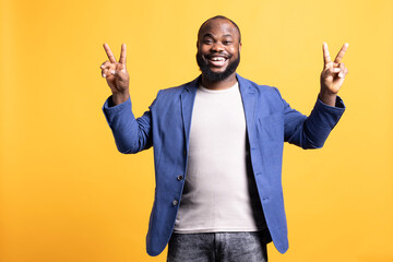 Portrait of joyous african american man doing victory sign and feeling happy, studio background....