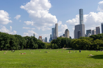 A sunny day in New York City’s park with skyscrapers in the background and people enjoying outdoor activities on the grassy field