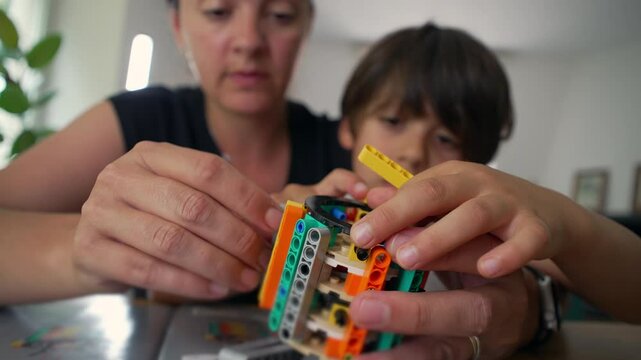 Close-up of mother and young boy’s hands working together on a building activity, carefully placing pieces, capturing a moment of collaboration and tactile learning