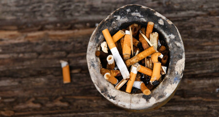 Closeup of an ashtray filled with numerous cigarette butts on a wooden surface, symbolizing smoking habits and litter, smoking harm, urban pollution, unhealthy lifestyle, littering.