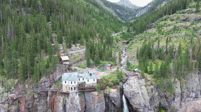 Powerhouse and Bridal Veil Falls near Telluride, Colorado. High angle flyover shot pushes in to show the structure, waterfall, cliffs and forest of the area.