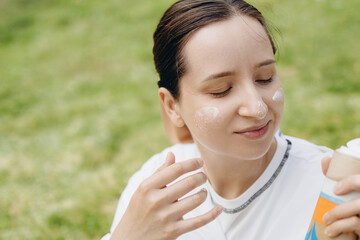 Young Woman Is Applying Sunscreen To Her Face On A Sunny Day, Ensuring Protection From The Sun's Rays