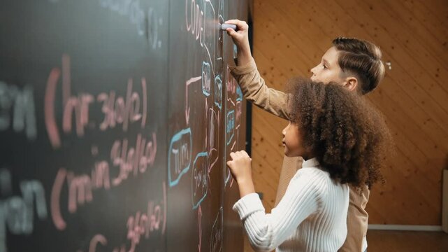 Diverse student brainstorm engineering prompt on blackboard. Group of happy children helping, support to create and design STEM technology classroom in casual cloth. Site view. Closeup. Erudition.