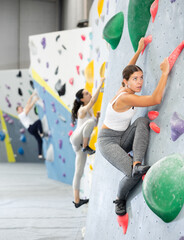 Fototapeta premium Young woman in sportswear practicing rock climbing on climbing wall