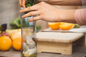 Healthy eating lifestyle concept photo of young woman preparing drink with fruit and vegetables at home in kitchen.
