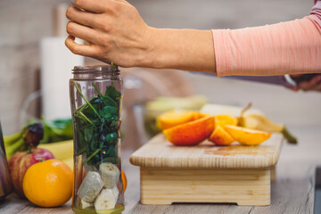 Healthy eating lifestyle concept photo of young woman preparing drink with fruit and vegetables at home in kitchen.