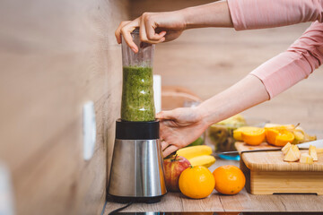 Healthy eating lifestyle concept photo of young woman preparing drink with fruit and vegetables at home in kitchen.