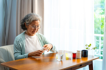 Asian senior mature woman patient taking medicine pill with drinking water from a glass for relief disease in bedroom Elderly retired woman taking vitamins complex supplement for self-care at home.