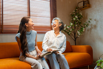 Asian senior mature woman reading a book with caregiver in living room. Happy elderly woman enjoy...