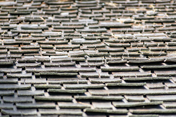 Aged wooden roof shingles with uneven layers and natural wear. Selected focus.