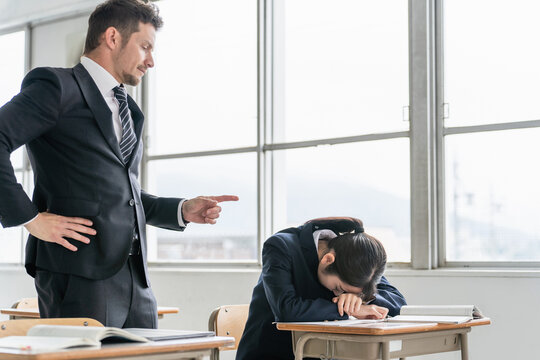 授業中に居眠りをする高校生と注意する先生
