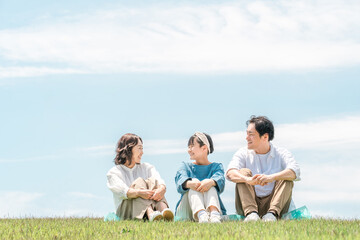 青空の見える公園・丘に座る家族・親子（父親・母親・娘）

