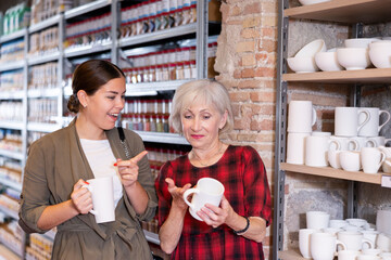 Elderly woman and young woman choose clay dishes in pottery shop