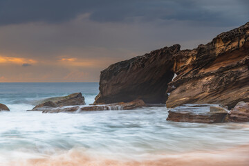 Obraz premium Sunrise at the seaside with rocks and beautiful diffused light by the rain clouds