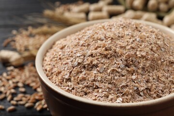 Bowl of wheat bran on black table, closeup