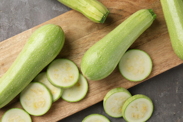 Board with fresh cut and whole zucchinis on grey textured table, flat lay