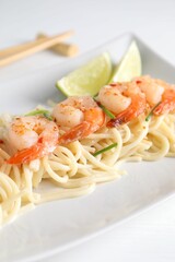 Delicious pasta with shrimps, green onions and lime on white table, closeup