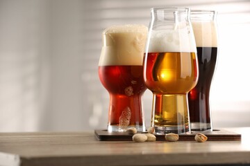 Glasses with different types of beer and pistachio nuts on wooden table indoors, closeup. Space for text
