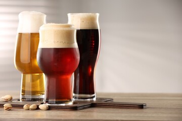 Glasses with different types of beer and pistachio nuts on wooden table indoors, space for text