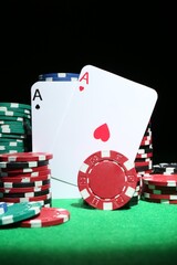 Obraz premium Playing cards and poker chips on green table against dark background