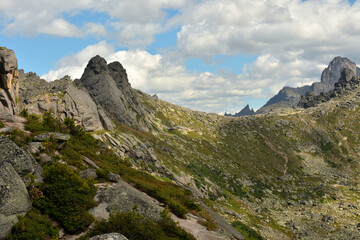 Hiking pass in the mountains with peaked rocks under a cloudy summer sky.