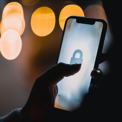 Close-Up of Smartphone Screen with Privacy Lock Icon, Emphasizing Phone Privacy, Blurred Silhouette Background, Hand Over Half the Screen