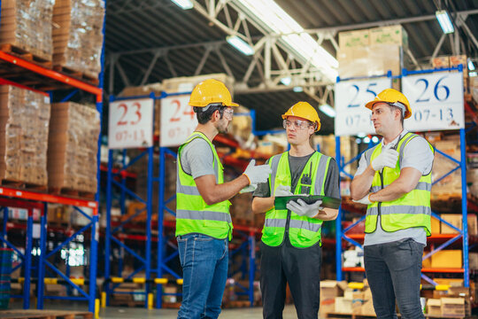 Three warehouse workers using a digital tablet while recording inventory. Logistics employees working with warehouse management software in a large distribution centre.
