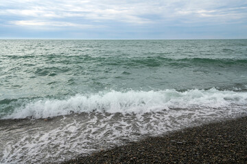 An incoming wave on the Black Sea and a pebble beach on the Sochi coast on a summer day with clouds, Sochi, Krasnodar Territory, Russia