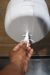 A hand is utilizing a paper towel dispenser located in a restroom for convenience and hygiene