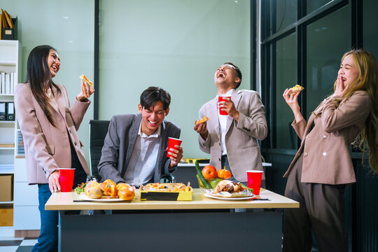 Four Asian friends, two men and two women, celebrate in an office party. They enjoy a fun-filled with food, drinks, and laughter, bonding over teamwork and friendship.