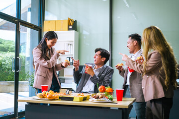 Four Asian friends, two men and two women, celebrate in an office party. They enjoy a fun-filled with food, drinks, and laughter, bonding over teamwork and friendship.