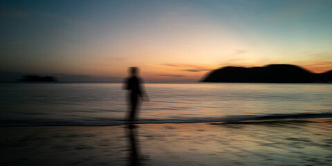 Sunrise beach and black silhouette people motion blur. Nature background sea, golden evening sky and blurred island.