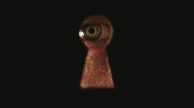 Male blue eye looking through the keyhole. The concept of voyeurism, curiosity, Stalker, surveillance and security