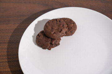 tres galletas achocolatadas con chispas en plato blanco sombre mesa de madera